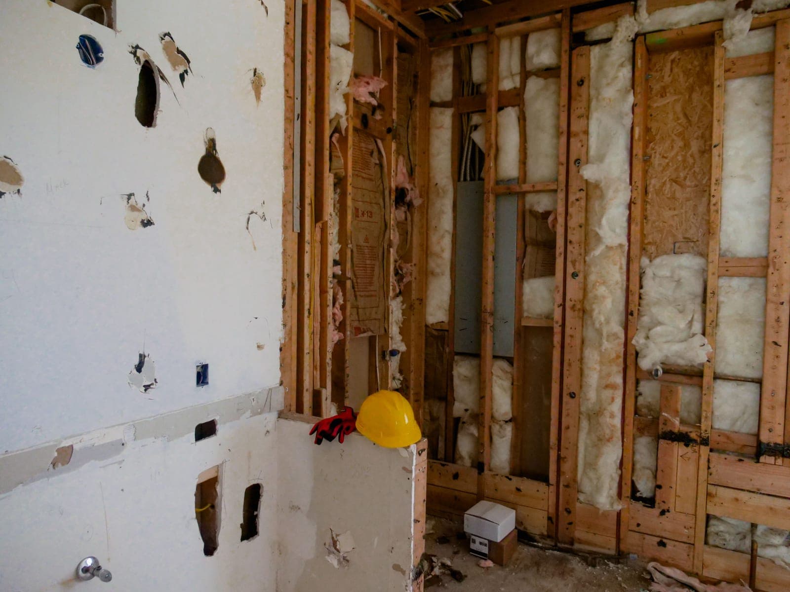 Interior stripped to the studs during a demolition, with a hard hat on a partial wall